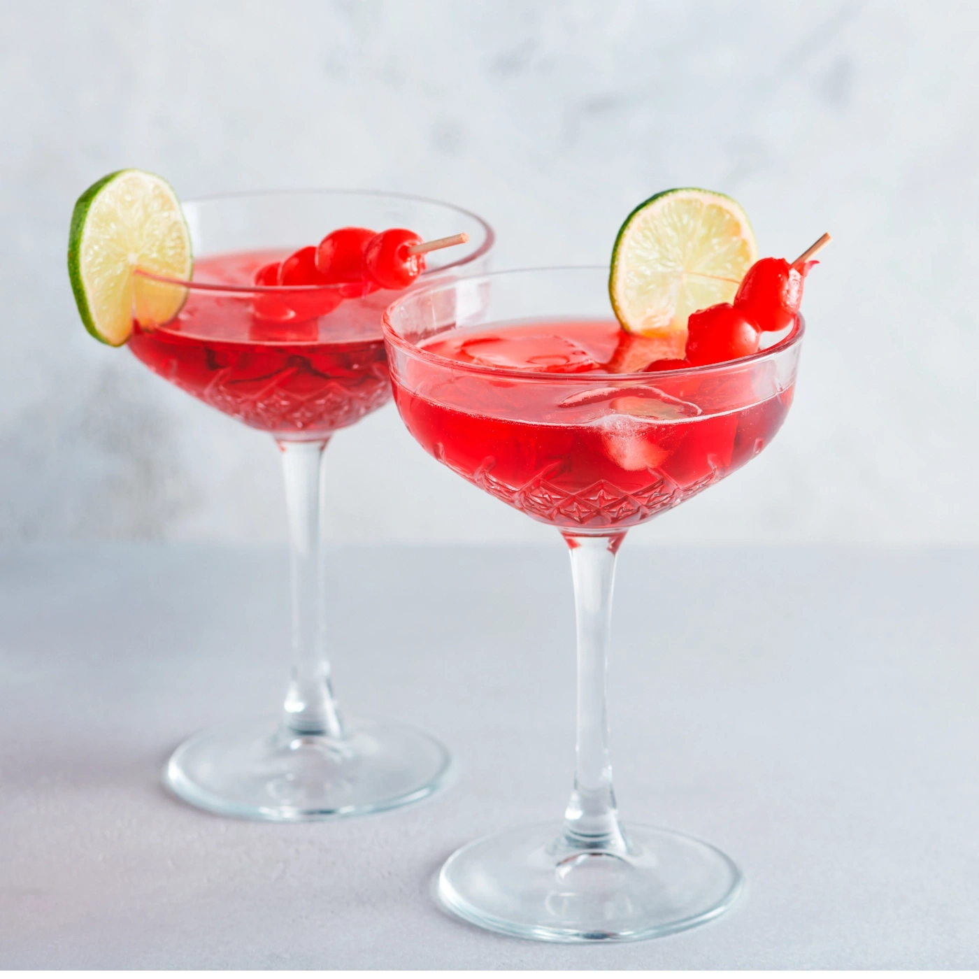 Zwei Cocktails mit Kirschen und Limettenscheiben auf einem Tisch.