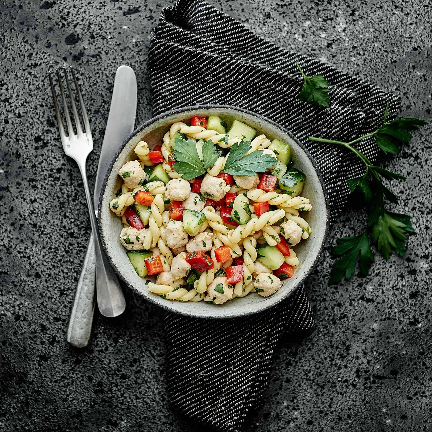 Nudelsalat mit Gemüse und Fleischbällchen in einer Schüssel mit Besteck und Serviette