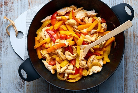 Hühnerpfanne mit Paprika und Zwiebeln in einer Pfanne mit Holzkochlöffel