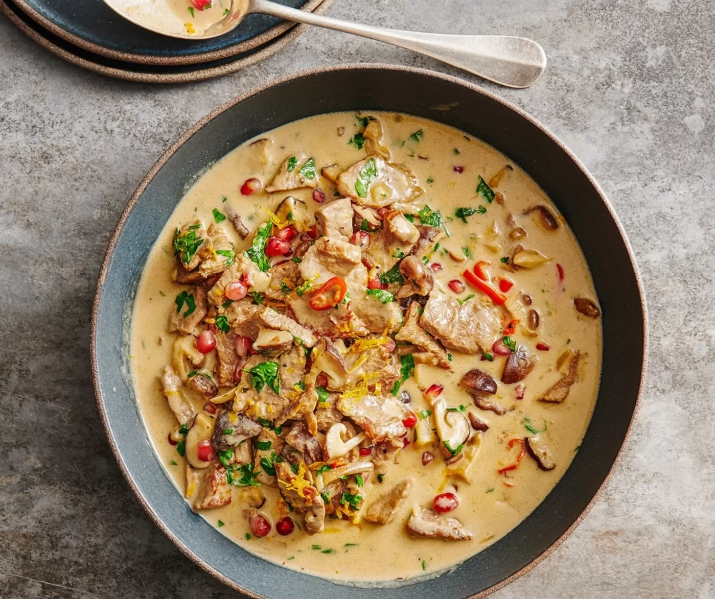 Un plat riche avec de la viande, des champignons, de la grenade et des herbes dans une sauce crémeuse.