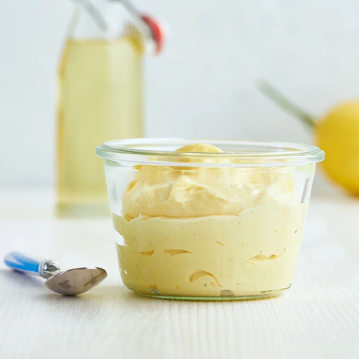 Un verre de crème jaune, une bouteille et une cuillère à côté.