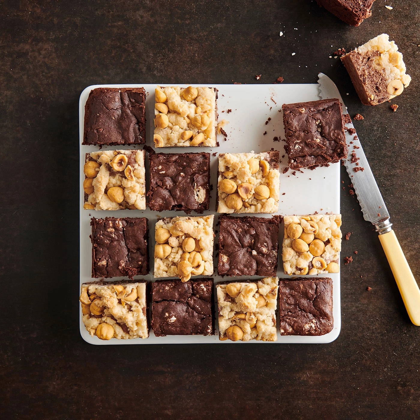 Brownies mit Nüssen auf einem weißen Tablett, daneben ein Messer.