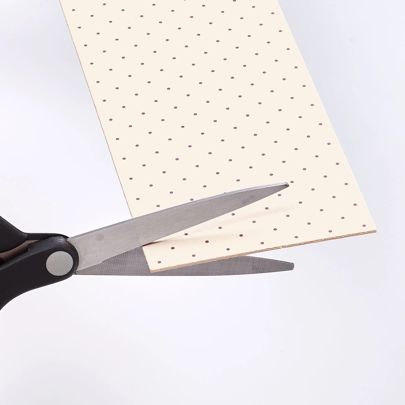 Ciseaux coupant du papier à pois sur fond blanc. Vue rapprochée.
