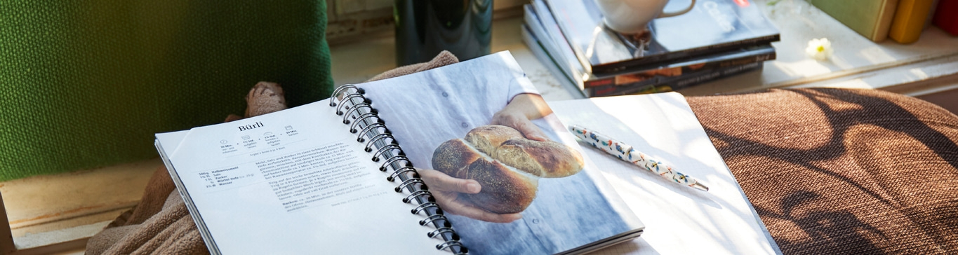 Kochbuch mit Rezept für Brot, Stift, Bücher, Kissen, Sonnenlicht, Nahaufnahme