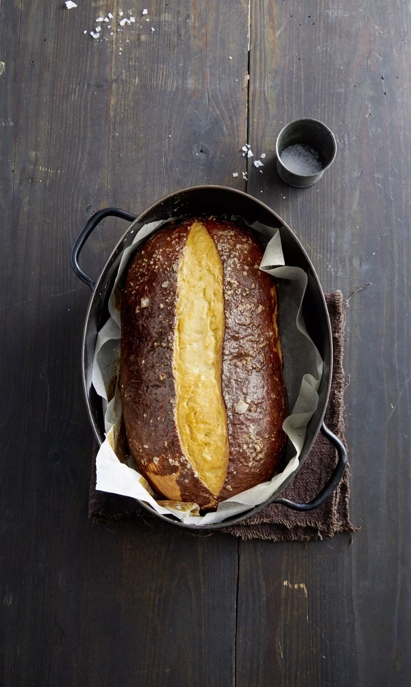 Ein Laib Brot mit grobem Salz und einem kleinen Metallbecher auf einem Holztisch.
