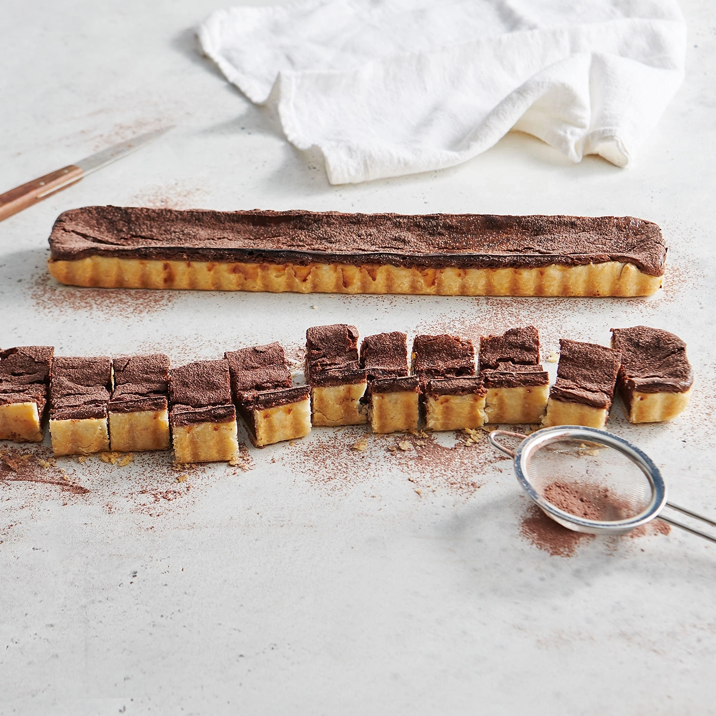 Schokoladenkuchen, geschnitten, auf einer weißen Oberfläche, mit einem Sieb.