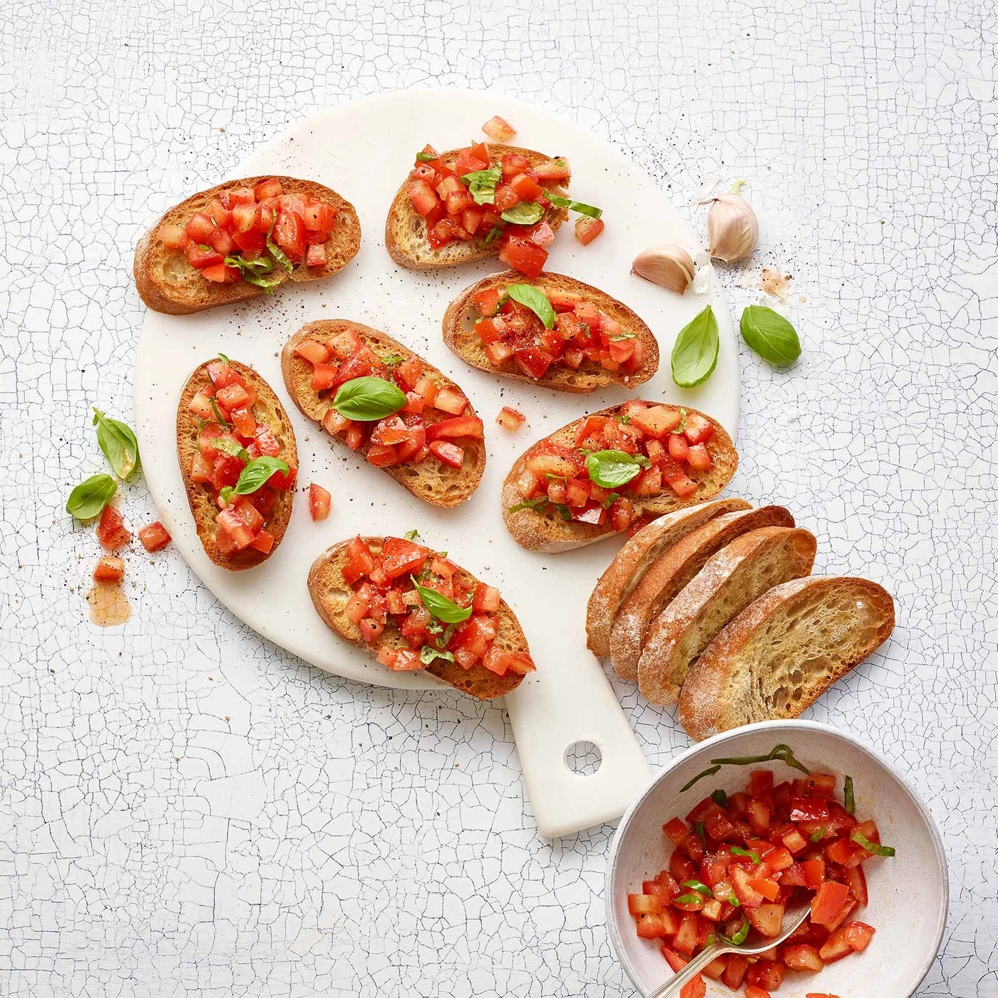 Bruschetta-Vorspeise mit Tomaten, Basilikum und Knoblauch auf einem weißen Brett.